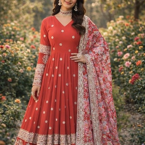 May include: A long, red dress with white polka dots and intricate gold embroidery on the sleeves and hem. A floral patterned shawl drapes over the shoulder. The dress has a V-neck and long sleeves.
