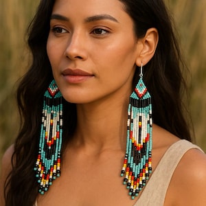 May include: Long beaded earrings with a Native American design. The earrings feature a turquoise, black, white, red, and yellow colour scheme. The earrings are made of small beads and hang down from the ear.