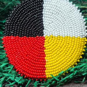 May include: A circular beaded patch featuring four distinct quadrants of color. The top left section is black, the top right is white, the bottom left is red, and the bottom right is yellow. Each quadrant is composed of small, uniform beads.