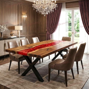 Op de afbeelding: Een houten eettafel met een levendige rode harsrivier in het midden. De tafel wordt ondersteund door zwarte metalen poten en is omgeven door bruine gestoffeerde stoelen. Boven hangt een kroonluchter.