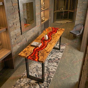 May include: A wooden dining table with a vibrant red resin river design. The table has a natural wood grain and sits on black metal legs. A white vase with flowers and a book are on the table.