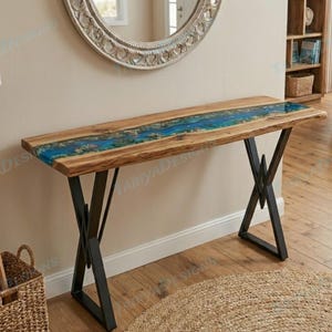 May include: A wooden console table with a blue resin river design. The table has a natural wood grain finish and black metal legs. The resin river detail runs down the center of the table, creating a unique and artistic look. The table is approximately 60 inches long.