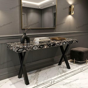 May include: A rectangular console table featuring a surface made of polished black and white agate slices with a natural geode pattern. The table is supported by a black metal X-shaped base and holds a black vase and a stack of three books.