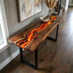May include: A wooden table with a river of orange and red resin. The table has a dark brown finish and black metal legs. The resin river glows with a fiery effect, creating a unique piece of furniture. The table is approximately 150 cm long.
