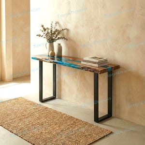 May include: A live edge console table with a blue epoxy resin river. The tabletop is supported by black metal legs. Decorative vases and books are on the table. A woven rug is on the floor.