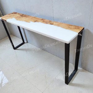 May include: A modern console table with a live edge wood top and white resin inlay. The table has black metal legs and measures approximately 60 inches long.
