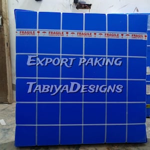 May include: A blue box with a grid pattern and the words "EXPORT PAKING" and "TABIYADESIGNS" in white. The box is sealed with red "FRAGILE" tape. The box is likely for shipping or storage.
