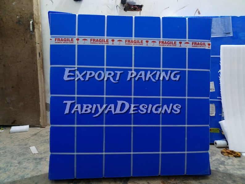 May include: A blue box with a grid pattern and the words "EXPORT PAKING" and "TABIYADESIGNS" in white. The box is sealed with red "FRAGILE" tape. The box is likely for shipping or storage.
