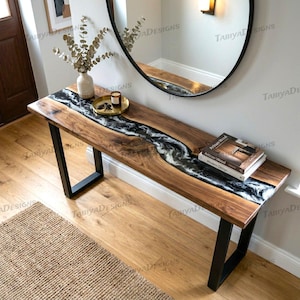 May include: A wooden console table with a black and white resin river design. The table has a dark wood finish, black metal legs, and a book on top. The text "TABIYADESIGNS" is visible.