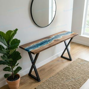May include: A wooden console table with a blue resin river design. The table has a dark wood finish and black metal legs. The resin river flows down the center of the table, creating a unique and artistic look. The table is 60 inches long.