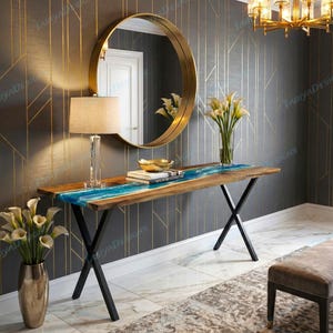 May include: A wooden console table with a blue resin river design. The table has black metal legs and is placed in front of a wall with a gold-colored geometric pattern. A gold-framed mirror hangs above the table.