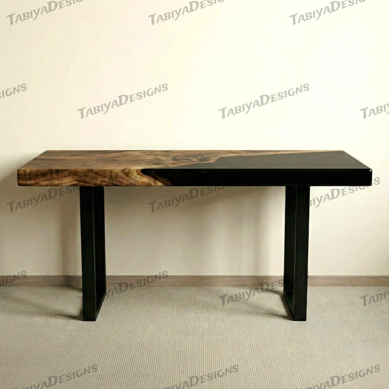 May include: A rectangular wooden table with a live edge and black epoxy resin. The table has a dark wood grain finish on one side and a glossy black finish on the other. It is supported by black metal legs.