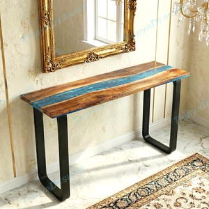May include: A wooden console table with a blue resin river design. The tabletop is supported by black metal legs. The table is approximately 48 inches long.