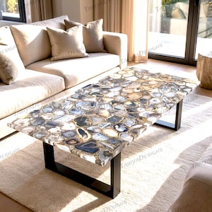 Puede incluir: Mesa de centro rectangular con una tapa de mosaico de piedra de ágata en tonos grises, azules y dorados. La mesa tiene una estructura de metal negro y está colocada sobre una alfombra de color claro. La mesa mide aproximadamente 122 cm de largo.