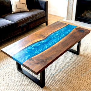 May include: A rectangular coffee table with a dark wood frame and a striking blue epoxy resin river running through the centre. The table is supported by black metal legs and sits on a light-coloured rug.