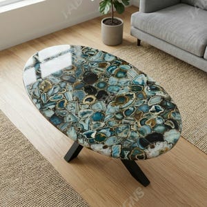 May include: An oval coffee table featuring a polished surface composed of numerous blue, teal, and brown agate stone slices. The table is supported by three black, angled metal legs, creating a stable base for the decorative stone tabletop.