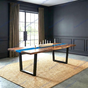 May include: A large, rectangular wooden dining table with a blue resin river down the center. The table has a live edge and sits on black metal legs. A beige rug is beneath the table. Candles and a decorative bowl are on the table.