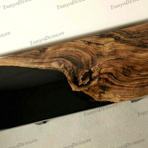 May include: A wooden slab with a dark resin inlay, showing intricate wood grain patterns in brown and tan hues. The resin provides a smooth, dark contrast. This piece could be a decorative item or part of a furniture design. The wood grain is highly detailed.