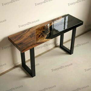 May include: A rectangular console table with a live edge wood top and a black epoxy resin section. The table has a black metal frame. The wood grain is visible. The table is approximately 152 cm long.