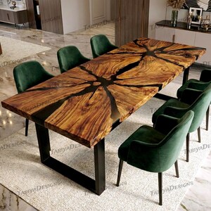 Op de afbeelding: Een grote, rechthoekige houten eettafel met een uniek ontwerp, met een donkere epoxyhars die de natuurlijke houtnerfpatronen opvult. De tafel wordt ondersteund door zwarte metalen poten en is omgeven door groene fluwelen stoelen.