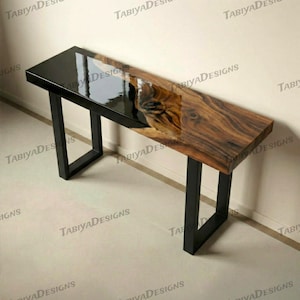 Puede incluir: Una consola rectangular con tapa negra y superficie de veta de madera natural. La mesa tiene patas de metal negro. La tapa mide aproximadamente 152 cm de largo y 38 cm de ancho.