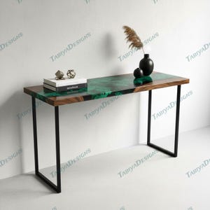 May include: A modern console table with a dark wood frame and a rectangular top. The tabletop features a striking green and black epoxy resin design. Decorative items include a black vase, a small sphere, and a stack of books.