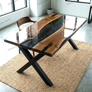 May include: A rectangular wooden table with a black epoxy resin river design. The table has a glossy finish and sits on black metal legs. The table is approximately 72 inches long and 36 inches wide.