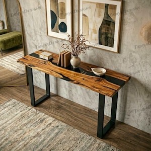 May include: A wooden console table with a live edge design and black resin inlay. The table has black metal legs and is decorated with books, a small dish, and a vase with dried branches. The table is approximately 60 inches long.