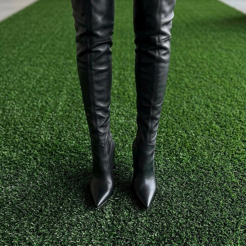 K&ouml;nnte beinhalten: Ein Paar schwarze Overknee-Stiefel mit glatter Oberfl&auml;che, spitzer Zehenpartie und einer vertikalen Naht entlang des Schafts. Die Stiefel reichen &uuml;ber das Knie, haben eine eng anliegende Passform und sind mit einem Stiletto-Absatz versehen.
