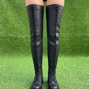 May include: A pair of black over-the-knee boots featuring a full-length front lace-up closure with thin black laces, a rounded toe, and a thick lug sole. The boots extend well above the knee and are constructed with a smooth, matte finish material.