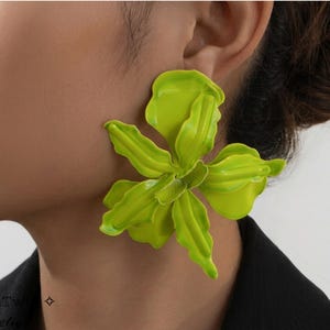 Puede incluir: Un pendiente único en forma de flor verde lima. El pendiente es de un color vibrante y sólido con formas de pétalos detalladas. La joya se lleva en la oreja, con el resto del cuerpo de la persona en el fondo.