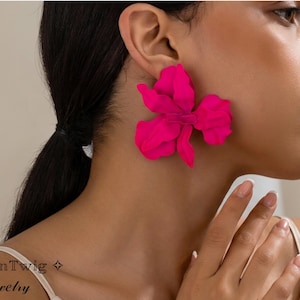 May include: Hot pink flower-shaped earrings. The earrings are large and bold, with a textured appearance. The jewelry is a statement piece, perfect for adding a pop of color to any outfit. The earrings are a vibrant accessory.