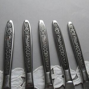 May include: Five silver flatware pieces with floral designs. The handles are decorated with a repeating pattern of flowers and leaves.