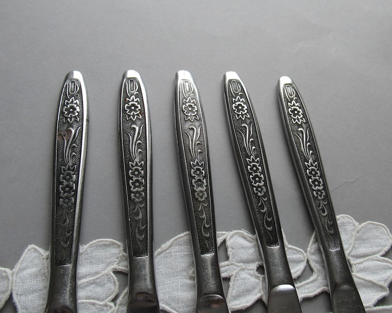 May include: Five silver flatware pieces with floral designs. The handles are decorated with a repeating pattern of flowers and leaves.