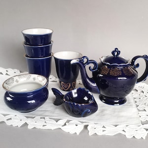 Puede incluir: Un juego de té azul y dorado con una tetera, cuatro tazas, un azucarero y un plato con forma de pez. El juego está decorado con motivos florales dorados.