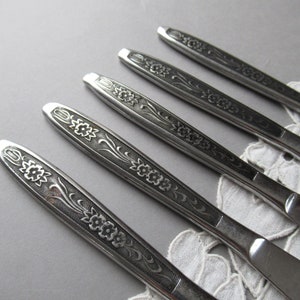 May include: Five silver dinner knives with floral designs on the handles.