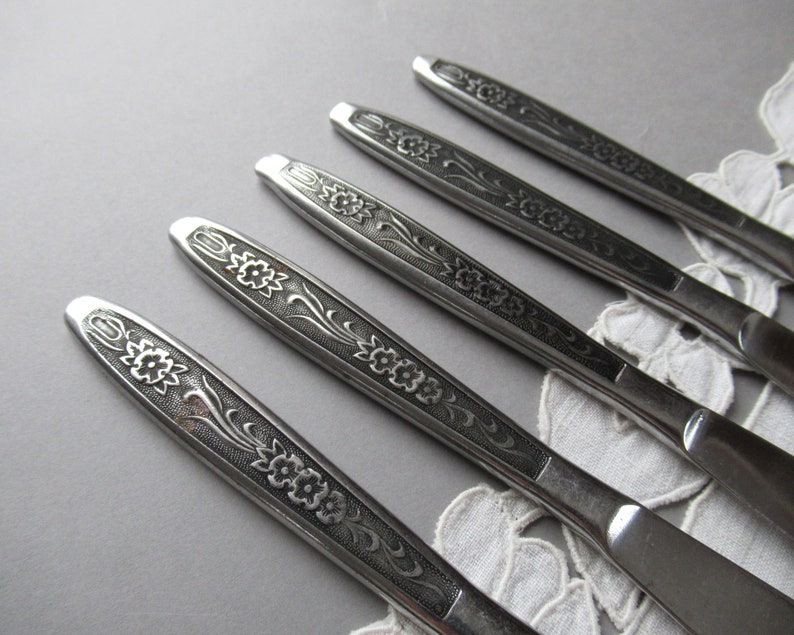 May include: Five silver dinner knives with floral designs on the handles.