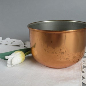 Könnte beinhalten: Eine Kupferschale mit gehämmerter Oberfläche. Die Schale ist leer und steht auf einer weißen Spitzentischdecke.