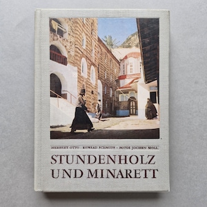 Może przedstawiać: Książka w twardej oprawie zatytułowana "STUNDENHOLZ UND MINARETT" ze zdjęciem sceny ulicznej na Bliskim Wschodzie. Na zdjęciu widać ludzi spacerujących w pobliżu kamiennego budynku z łukowatymi oknami i czerwoną kopułą. Książka ma jasnoszarą lnianą okładkę.