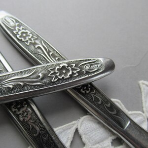 May include: Close-up of three silver flatware pieces with an ornate floral design. The handle of one piece has the word "HENRY" engraved on it.