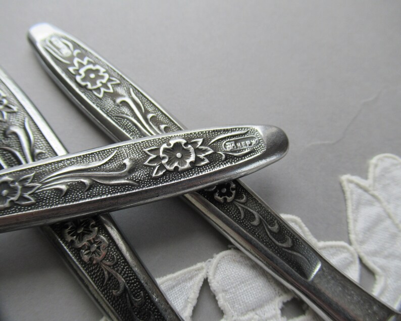 May include: Close-up of three silver flatware pieces with an ornate floral design. The handle of one piece has the word "HENRY" engraved on it.