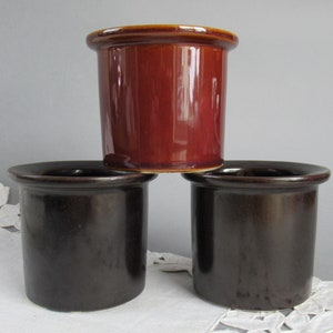 Pode incluir: Três recipientes de cerâmica em tons de castanho. O recipiente superior é um castanho avermelhado rico, enquanto os dois inferiores são um castanho chocolate mais escuro. Cada um tem uma forma cilíndrica com uma borda ligeiramente alargada.