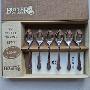 Puede incluir: Un juego de seis cucharillas de café plateadas en una caja marrón. Las cucharas están dispuestas en fila. La caja tiene texto que dice "Butler Cutlery", "Dubarry" y "Made in Sheffield, England".