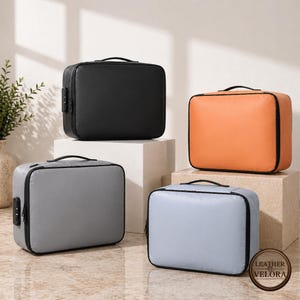 May include: Four rectangular document cases in black, orange, grey, and light blue. Each case has a black handle and a combination lock. The cases are displayed on neutral-coloured pedestals, with a plant in a vase in the background.