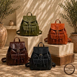 May include: Four leather backpacks in olive green, brown, black, and rust orange. Each backpack has a flap closure with a buckle, drawstring, and side pockets. The backpacks are displayed on stone blocks.