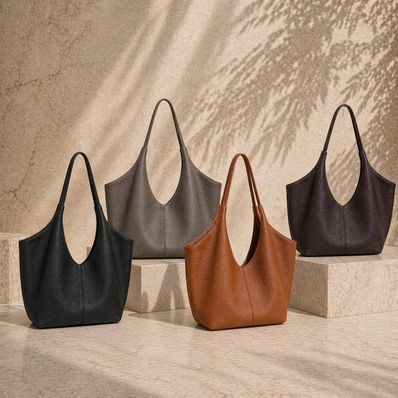 May include: Four leather tote bags in black, gray, brown, and tan. Each bag has a wide, open top and a single, long handle. The bags are displayed on a neutral background with subtle shadows.