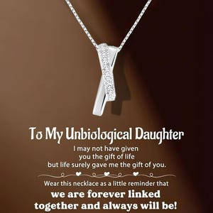 May include: A silver necklace featuring an X-shaped pendant embellished with small, sparkling stones. The necklace is displayed against a brown backdrop with the text "To My Unbiological Daughter" and a heartfelt message.