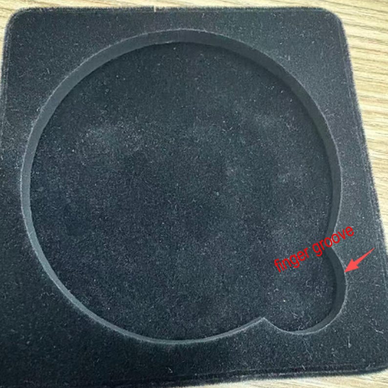 Puede incluir: Inserto negro de forma cuadrada con una hendidura circular y una ranura para los dedos. El inserto est&aacute; hecho de un material suave y aterciopelado, y la hendidura circular est&aacute; delineada con un borde elevado.