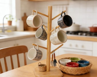 May include: A bamboo mug tree holds six ceramic mugs with various patterns and colors. A small woven basket and a basket with colorful bowls sit on a wooden table. Kitchen utensils hang from the tree.