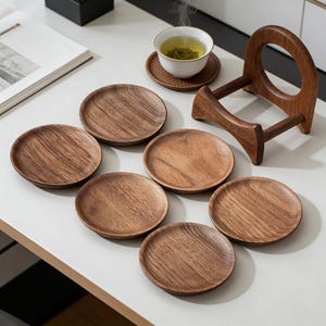Könnte beinhalten: Ein Set aus sieben runden Untersetzern aus Holz mit einem natürlichen Holzmaserungsmuster. Eine Tasse Tee steht auf einem passenden Untersetzer, mit einem hölzernen Tassenhalter im Hintergrund. Die Untersetzer sind auf einer weißen Oberfläche angeordnet.